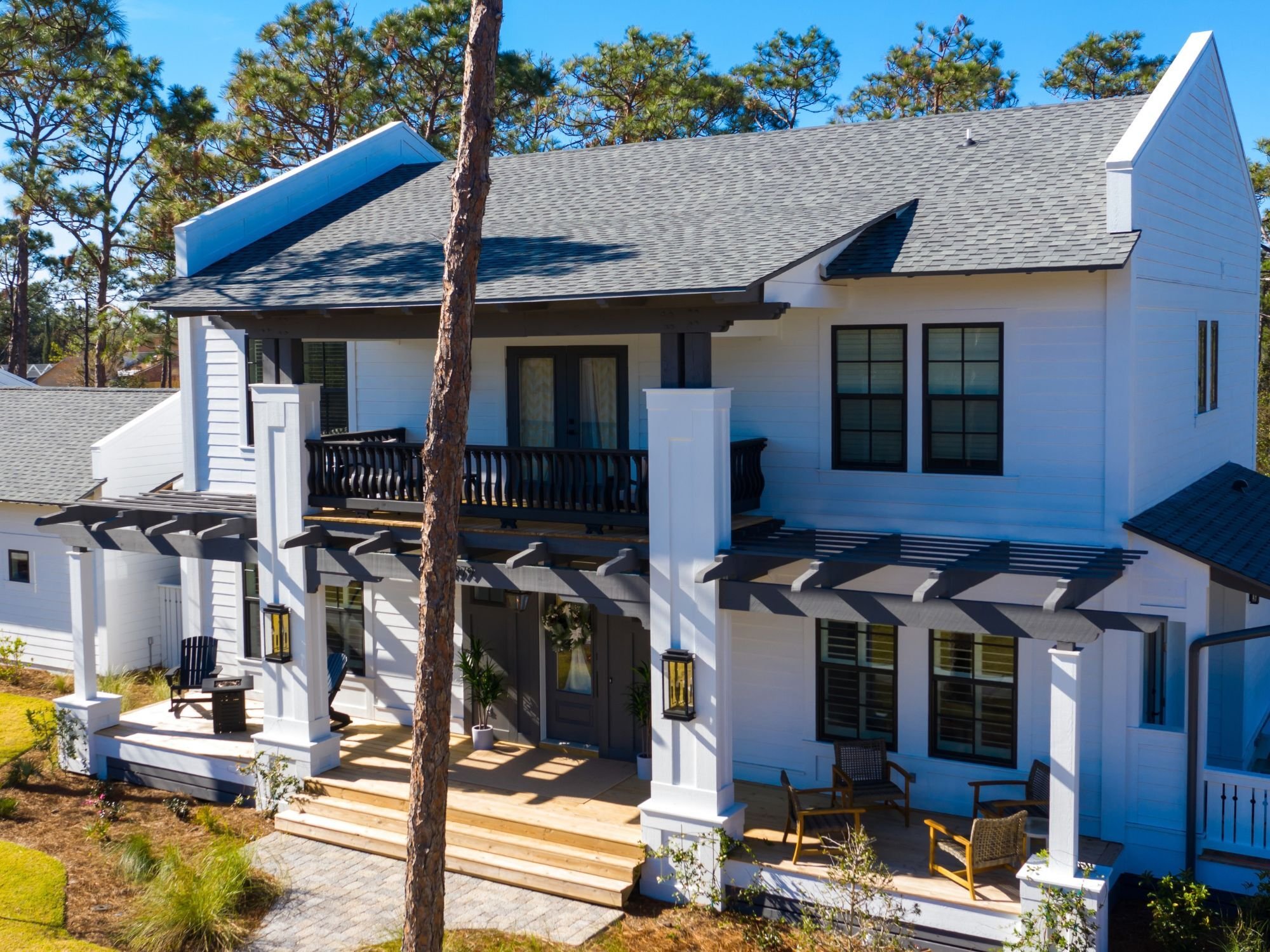 Exterior of a custom home in Leeward by Urban Infill featuring a white two-story exterior, dark bronze windows, exposed timber, parapet end walls, deep porches, and a centered second-floor balcony Exterior of a custom home in Leeward by Urban Infill featuring a white two-story exterior, dark bronze windows, exposed timber, parapet end walls, deep porches, and a centered second-floor balcony