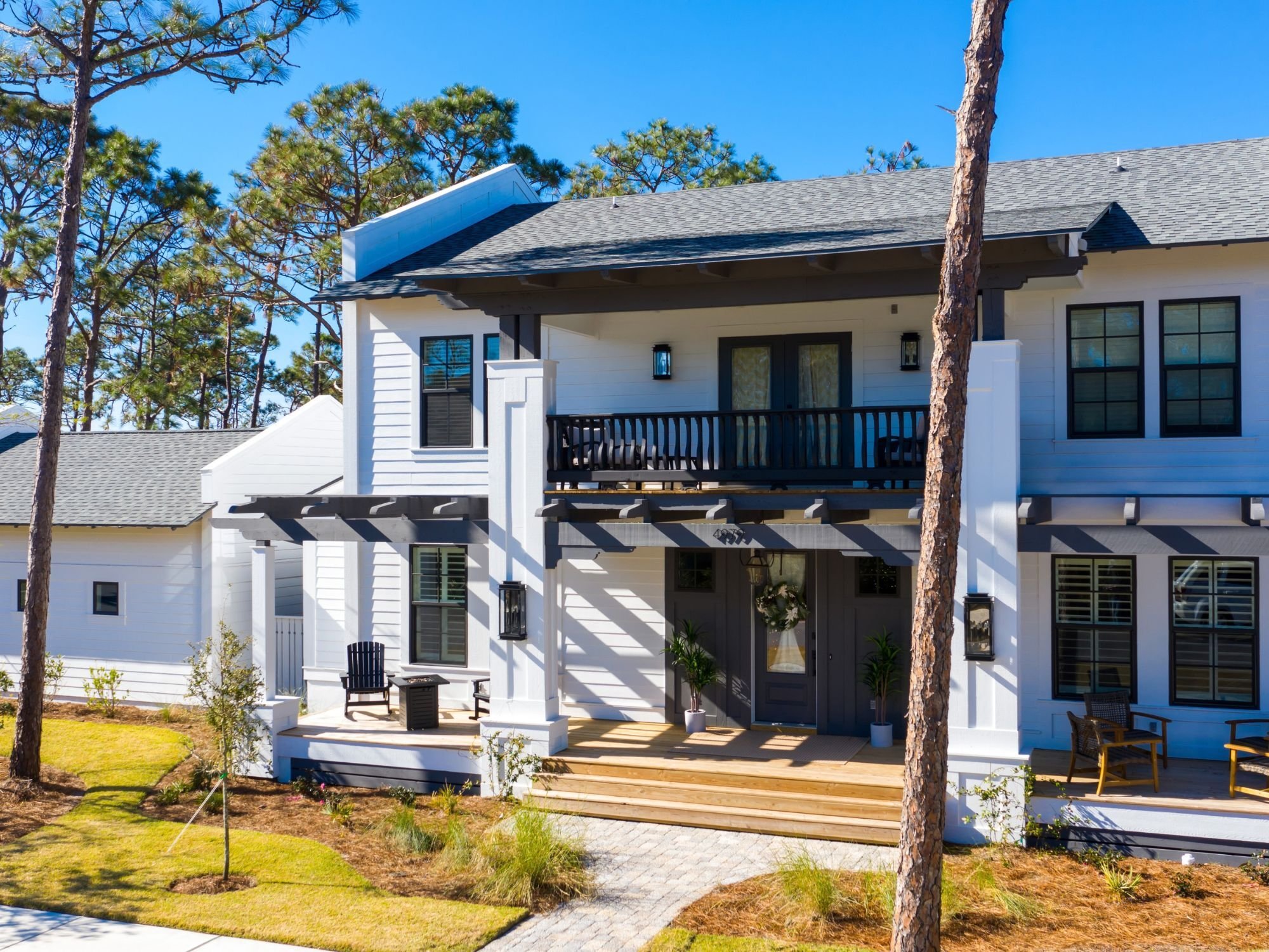 Leeward custom home with a white two-story exterior, dark bronze windows, exposed timber, parapet end walls, deep porches, and a centered second-floor balcony by Urban Infill in Pensacola, FL Leeward custom home with a white two-story exterior, dark bronze windows, exposed timber, parapet end walls, deep porches, and a centered second-floor balcony by Urban Infill in Pensacola, FL