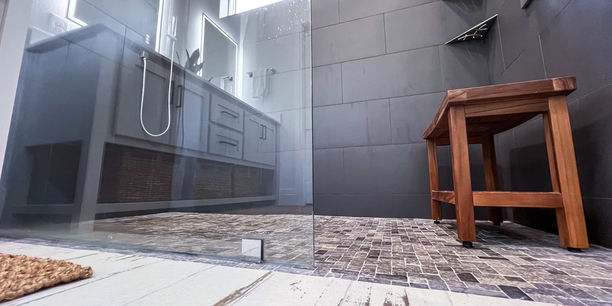 Spa-like walk-in shower with wooden seat, stone flooring, dual vanity in a custom home by Urban Infill