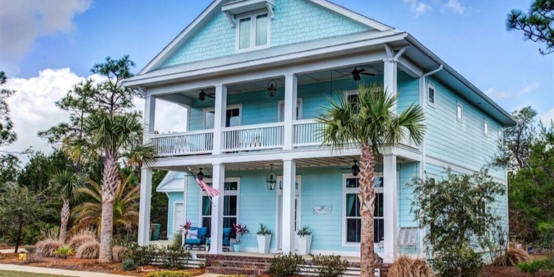 Two-story coastal blue home in Pensacola with palm trees and double porch by Urban Infill