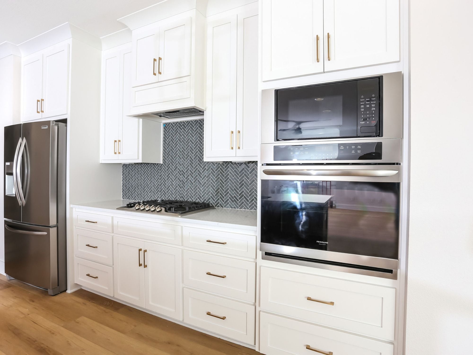 Custom kitchen in a Leeward custom home with stainless steel appliances, white cabinetry, and a herringbone tile backsplash above a gas cooktop by Urban Infill in Pensacola, FL