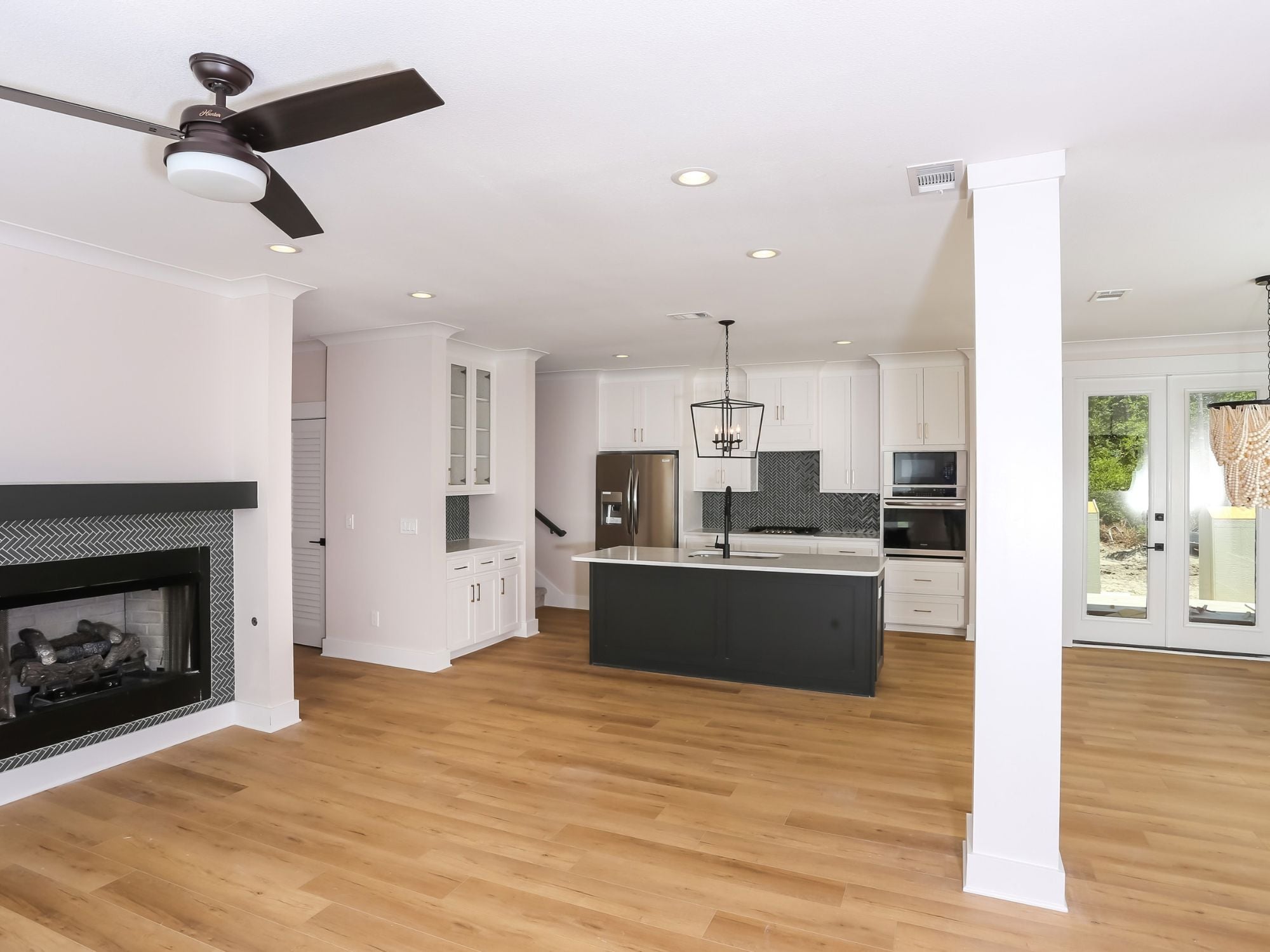 Open-concept living area and kitchen in a Leeward custom home with a fireplace, custom cabinetry, and a kitchen island by Urban Infill in Pensacola, FL
